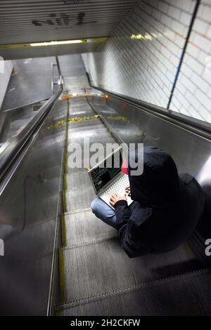 Image symbolique piratage informatique, cybercriminalité, cyberattaque, pirate avec ordinateur portable dans une station de métro, Banque D'Images