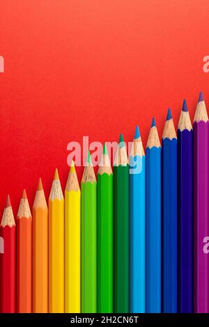 Crayons de couleur disposés en diagonale sur un fond de papier vertical rouge. Banque D'Images