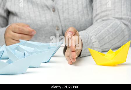 bateaux en papier entre une main femelle sur une table blanche.Concept de solution de conflit, négociateur entre les groupes.Recherche de décisions Banque D'Images