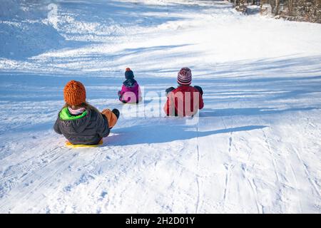 Trois enfants heureux sur une colline avec des traîneaux en plastique. Banque D'Images