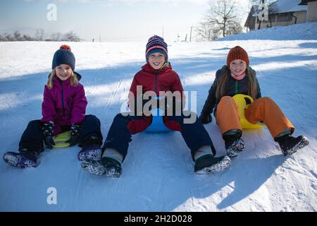 Trois enfants heureux sur une colline avec des traîneaux en plastique. Banque D'Images