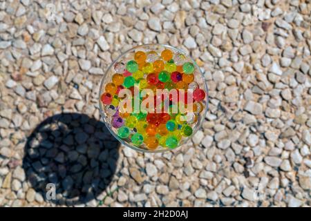 photo d'une tasse en verre placée sur un sol en galets, remplie de perles de couleur (orbis) avec mise au point sélective Banque D'Images