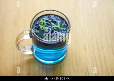 Une tasse en verre transparent de thé aux pois bleu papillon sur une table en bois. Banque D'Images