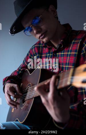 Beau homme hispanique portant un chapeau et des lunettes jouant de la guitare Banque D'Images