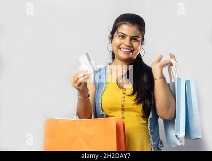 Une belle femme indienne en robe jaune avec des sacs de shopping et une carte de crédit sur fond blanc Banque D'Images