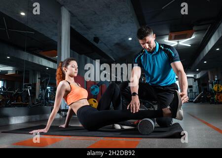 jeune femme se détendant avec un rouleau de relâchement myofascial avec entraîneur dans la salle de gym Banque D'Images