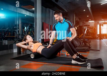 jeune femme se détendant avec un rouleau de relâchement myofascial avec entraîneur dans la salle de gym Banque D'Images