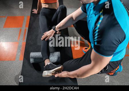 jeune femme se détendant avec un rouleau de relâchement myofascial avec entraîneur dans la salle de gym Banque D'Images