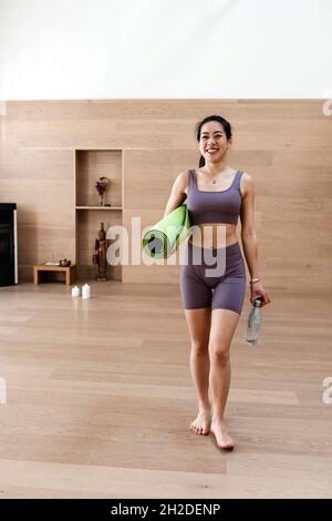 Femme asiatique en costume d'entraînement est tenue tapis de yoga et de bouteille Banque D'Images