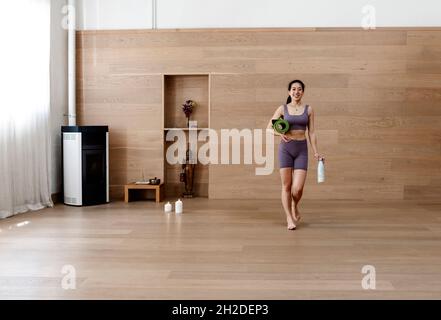 Femme asiatique en costume d'entraînement est tenue tapis de yoga et de bouteille Banque D'Images