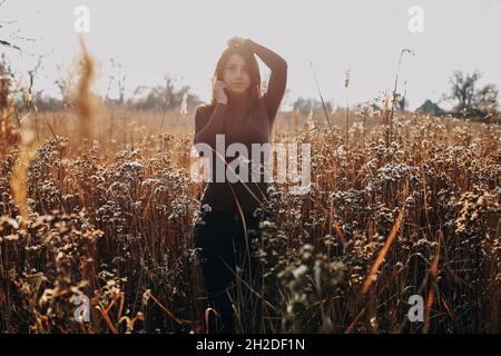 Stand de fille dans l'herbe sèche champ d'automne dans la tenue décontractée, couleurs neutres Banque D'Images