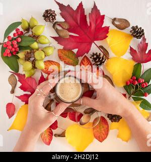 Tasse à café sur fond de feuilles d'automne jaunes et rouges avec la main d'une femme Banque D'Images