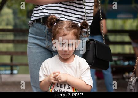 Une petite fille gaie avec des queues de cheval se tient devant sa mère dans la rue Banque D'Images