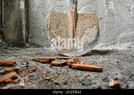 des couleurs vertes existent sur le côté métallique de la pelle, travaux de construction. photo prise pelle à angle bas devant le mur récemment fait plâtré par le béton. Banque D'Images