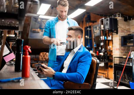 Un homme taillé sa barbe dans un salon de coiffure professionnel Banque D'Images