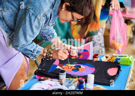 Svetlogorsk, Russie - 08.14.2021 - artiste féminine peignant sur un T-shirt noir à l'aide d'une brosse et d'une peinture textile.Créez votre propre tee-shirt, relooking for Tun Banque D'Images