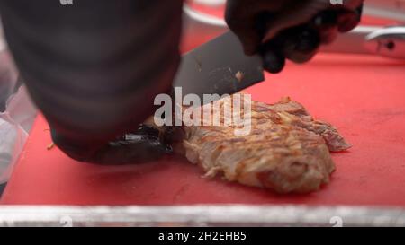 Chef en gants noirs coupe des steaks de viande juteuse sur la planche à bois avec le couteau, gros plan.Délicieux, juteux, viandes fraîchement cuisinées steaks cuisent des coupes sur le c Banque D'Images