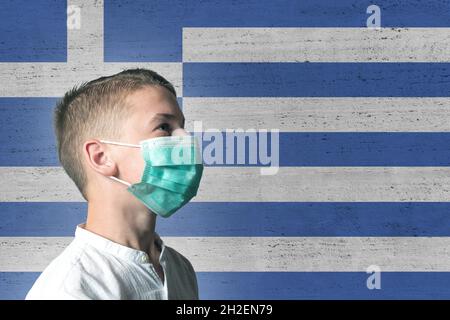 Garçon dans un masque médical sur son visage sur fond de drapeau de la Grèce.Virus épidémique 2019-nCoV syndrome respiratoire.Concept de médecine. Banque D'Images