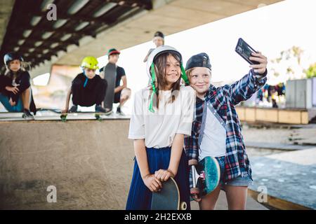 Les adolescents au skate Park s'amusent ensemble.Deux jeunes filles élégantes qui prennent une photo de selfie au téléphone tout en posant sur la rampe du parc de skate de la rue Banque D'Images