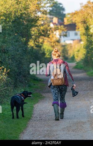 une jeune femme qui marche un chien noir le long d'une ruelle de campagne sur l'île de wight porte un sac de croque-chien. une jeune femme avec un chien qui marche le long de la ruelle de campagne. Banque D'Images