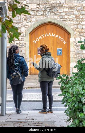 Deux femmes noires ou B A M E qui parlent debout à un arrêt d'autobus ou à un abri qui parle dans la ville de southampton; deux femmes de couleur qui attendent un autobus Banque D'Images