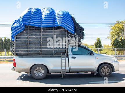 Un pick-up porte un tas recouvert d'une grande toile, la Thaïlande. Banque D'Images