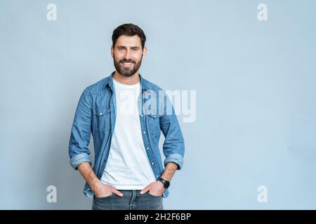 Beau jeune homme isolé sur fond bleu regardant la caméra et souriant Banque D'Images
