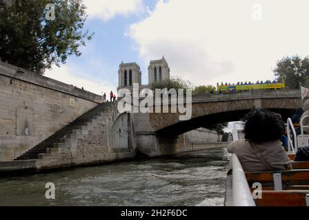 Seine, Paris, France avec bateau sur le point de passer sous le petit Pont et bus à toit ouvert passant par le pont et haut de la cathédrale notre-Dame visible Banque D'Images