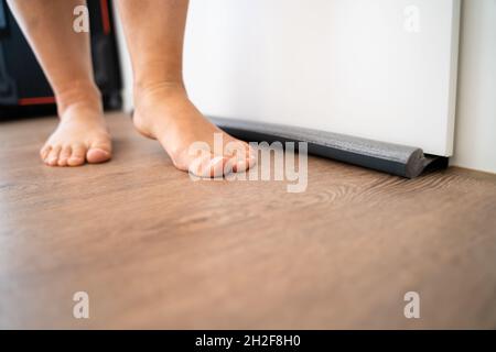 Personne marche pieds nus près de projet joint sous porte bloque l'air froid de voyager autour de Banque D'Images