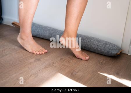 Personne marche pieds nus près de projet joint sous porte bloque l'air froid de voyager autour de Banque D'Images