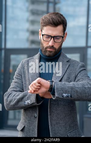 Homme d'affaires très occupé regardant la montre-bracelet tout en se précipitant sur le stand de réunion à l'extérieur Banque D'Images