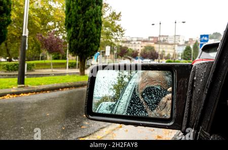 homme se focalisant avec une caméra sur le rétroviseur de sa propre voiture pleine de gouttes d'eau de pluie Banque D'Images