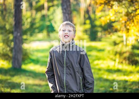 L'adolescent rit en ouvrant ses dents dans un parc de la ville sur fond de feuillage d'automne Banque D'Images