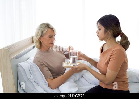 Fille asiatique prenant soin de sa mère malade au lit.La femme âgée prend des médicaments avec de l'eau pour améliorer son état de santé. Banque D'Images