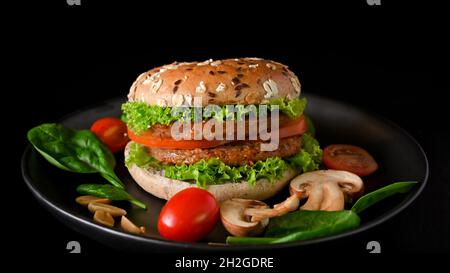 Gros plan de la nourriture américaine de junk dans les ingrédients à base de plantes, hamburger de viande de vegan juteux grillé avec des légumes à haute fibre sur fond noir. Banque D'Images