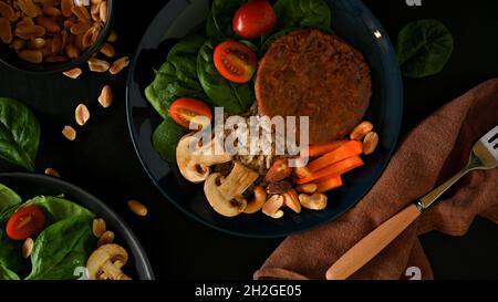 Vue de dessus du hamburger aux protéines de soja sur du riz brun avec des épinards, des tomates, des champions, des carottes et des noix sur une assiette.Repas végétalien à base de plantes. Banque D'Images