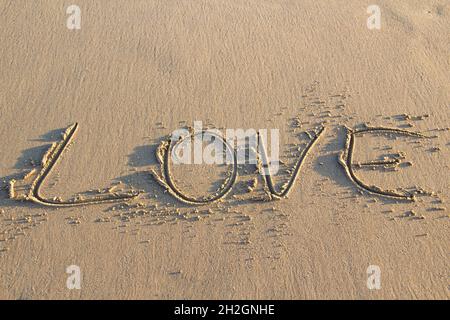 Mot AMOUR écrit sur le sable sur la plage contre fond.Concept de dessin de lettres sur le sable. Banque D'Images