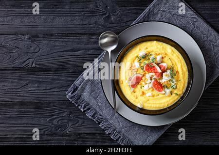 Soupe à la crème de potiron au thym servie dans un bol noir avec féta et figues servies sur un fond en bois avec une cuillère, vue du dessus, gros plan Banque D'Images