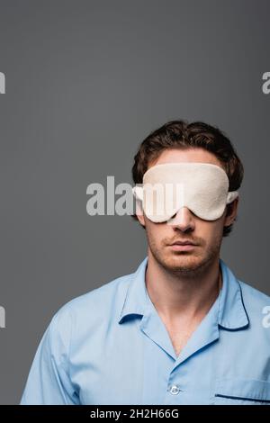 Jeune homme en pyjama et masque de sommeil isolé sur le gris Banque D'Images