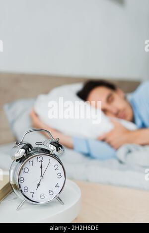 Réveil et livre sur table de chevet près de brouillé homme dormant sur le lit Banque D'Images