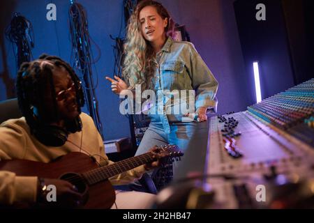 Jeune joli chanteur chantant pendant que l'homme joue de la guitare ils enregistrent une chanson dans le studio Banque D'Images