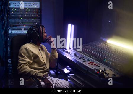 Un jeune homme africain écoute de la musique dans un casque, assis au clavier musical du studio Banque D'Images