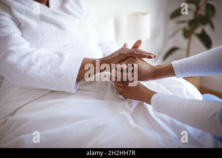 Femme afro-américaine médecin tenant les mains d'une patiente sénior à la maison Banque D'Images