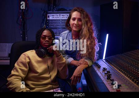 Portrait d'une jeune chanteuse avec son producteur de musique regardant l'appareil photo tout en travaillant dans un studio d'enregistrement numérique Banque D'Images