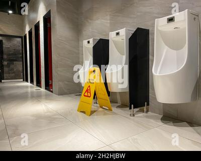 Mouiller l'affiche de sol près de la zone des urinoirs dans les toilettes publiques pendant le processus de nettoyage Banque D'Images