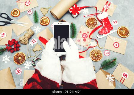 Mains du Père Noël avec un téléphone.Préparation du calendrier de l'Avent.Tradition de Noël saisonnière.Flat lay, vue de dessus. Banque D'Images
