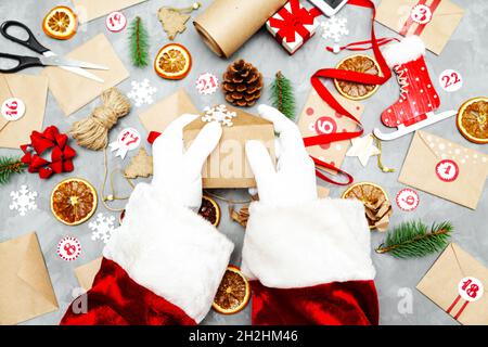 Le Père Noël prépare le calendrier de l'Avent.Enveloppes éco-artisanales avec cadeaux pour enfants.Tradition de Noël saisonnière.Flat lay, vue de dessus. Banque D'Images