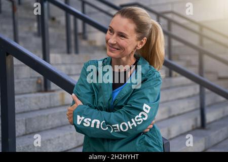 Portrait d'une sportive joyeuse d'âge moyen dans des vêtements de sport souriant de côté en se tenant à l'extérieur après l'entraînement dans la ville Banque D'Images