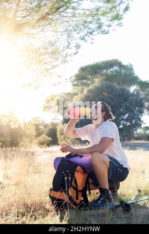 Eau potable de randonneur soif dans la campagne.Le randonneur laisse son sac à dos et ses bâtons sur le sol pour se rafraîchir Banque D'Images