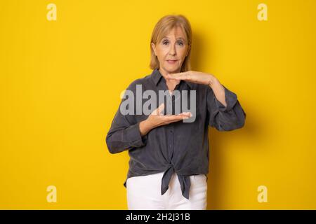 Femme âgée montrant l'espace produit avec les mains isolées sur fond jaune. Banque D'Images